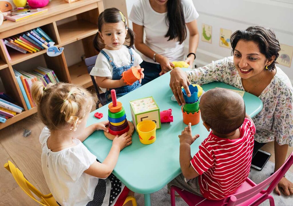 An educator at a table with four toddlers and stacking toys